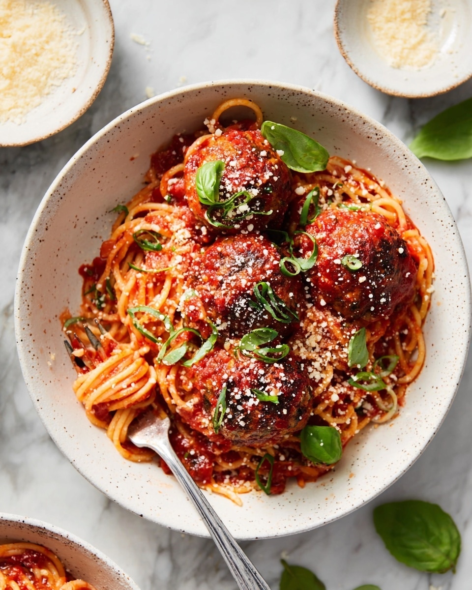 A black pan filled with about twelve round meatballs fully covered in thick, chunky bright red tomato sauce. The meatballs are dark brown with a slightly crispy texture and are topped with small green basil leaves and thinly sliced basil strips. Light brown grated cheese is scattered over the meatballs and sauce. A silver spoon is scooping one meatball on the right side of the pan. The pan rests on a white marbled surface with some basil leaves and a white cloth near the handle. Photo taken with an iphone --ar 4:5 --v 7