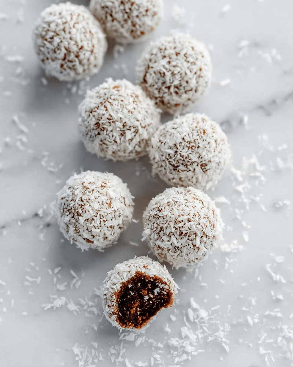 The image shows small round chocolate balls covered with white coconut flakes, each placed in a white paper cup. The chocolate balls have a rough texture with visible bits inside and a dark brown color peeking through the coconut flakes. The paper cups form a neat layer underneath each ball, sitting on a smooth white marbled surface. Several chocolate balls are scattered in the background, softly out of focus, emphasizing the single ball in the front. photo taken with an iphone --ar 4:5 --v 7