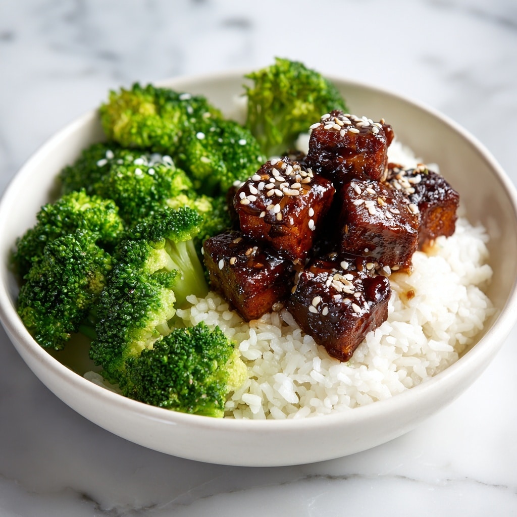 A white bowl holds a three-part dish on a white marbled surface: bright green cooked broccoli on the left, a bed of fluffy white rice in the center and bottom right, and on top of the rice, dark brown glazed tofu cubes stacked in a small pile, coated in a glossy sauce and sprinkled with white and black sesame seeds for texture and contrast. photo taken with an iphone --ar 4:5 --v 7