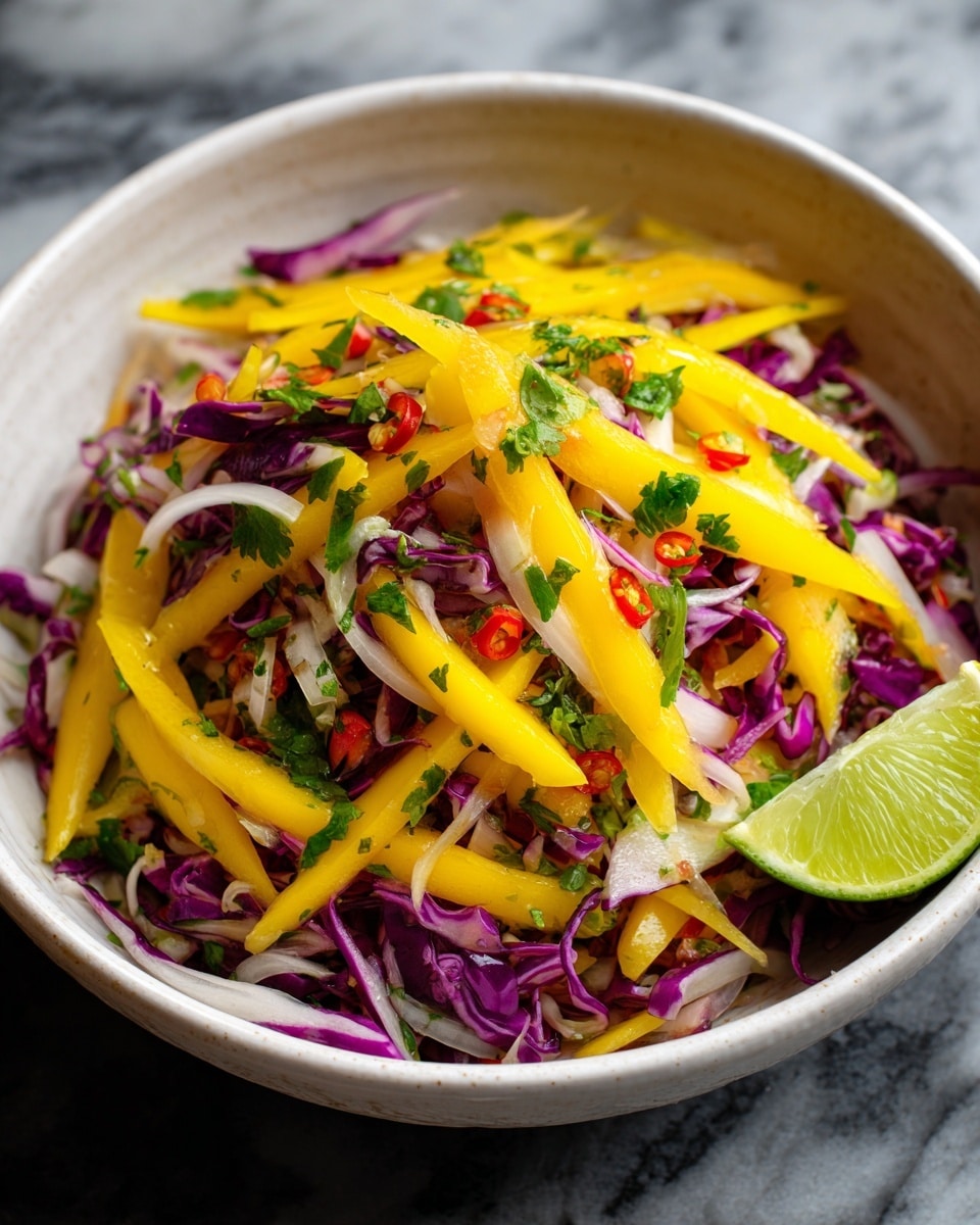 A close-up view of a fresh salad in a white bowl showing yellow mango strips layered on top of thin purple cabbage and small white onion slices, all mixed with bits of red chili and bright green chopped herbs, with a lime wedge resting on the edge of the bowl to the right. The textures vary from soft mango to crunchy cabbage, creating a colorful, vibrant mix against a white marbled background. photo taken with an iphone --ar 4:5 --v 7