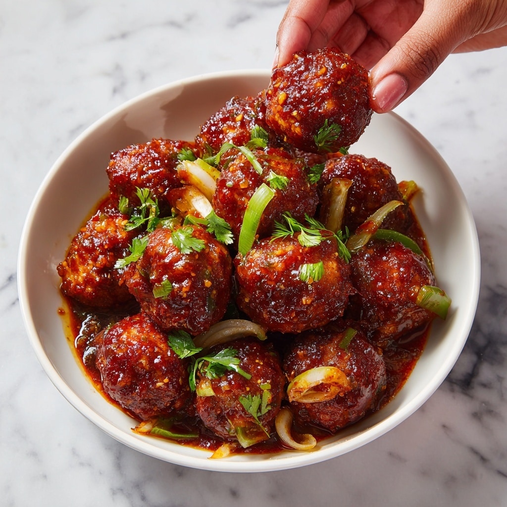 A white bowl filled with around fifteen deep-fried cabbage balls coated in a shiny, reddish-brown sauce, scattered with small pieces of chopped green onions and thin green pepper slices beneath the balls, all sitting on a bed of thick sauce with visible bits of vegetables. A woman's hand is holding one of the cabbage balls above the bowl. The scene is set on a white marbled surface. photo taken with an iphone --ar 4:5 --v 7