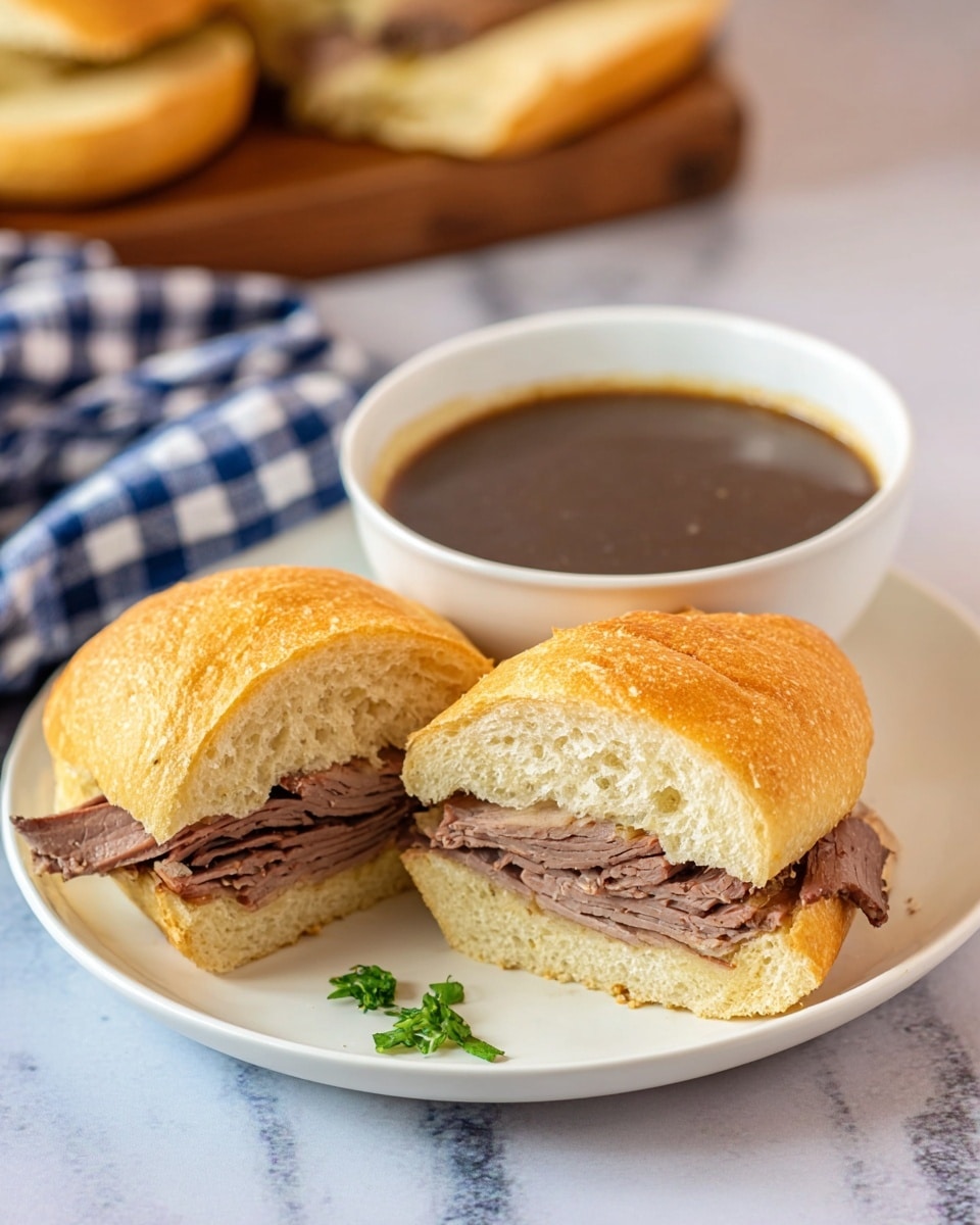 A close-up view of a sandwich cut in half, showing soft, light beige bread with a crusty top and inside filled with thin, folded slices of brown roasted meat layered neatly. The sandwich sits on a white plate with a small white bowl next to it filled with dark brown broth, slightly textured on top with small green garnish. The background features a white marbled texture with a green leafy herb blurred in the back. photo taken with an iphone --ar 4:5 --v 7