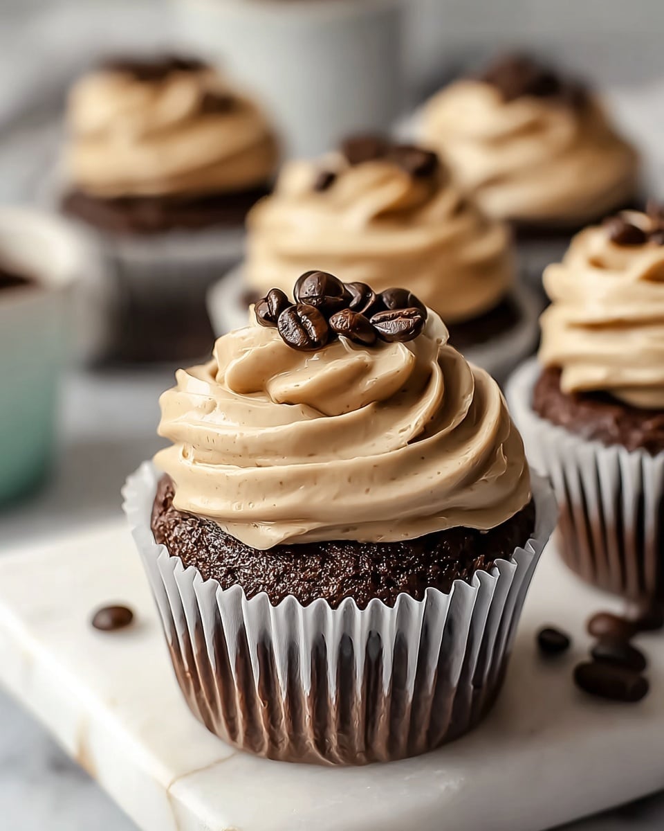 A close-up of a chocolate cupcake with three clear layers: the bottom layer is dark brown, moist chocolate cake, wrapped in a white cupcake liner; the middle layer is a thick swirl of light brown, creamy coffee-flavored frosting with a smooth texture, covering the top of the cake; the top layer is a small pile of dark, shiny coffee beans placed in the center of the frosting. The cupcake sits on a white marble plate, surrounded by more identical cupcakes in the background. The background also shows a white marbled texture. photo taken with an iphone --ar 4:5 --v 7
