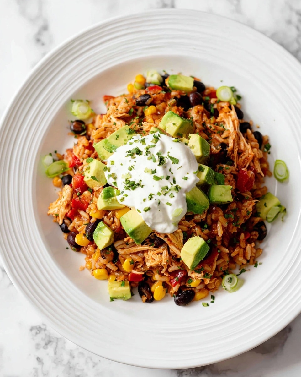 A white ridged plate holds a colorful layered dish starting with a base of shredded chicken mixed with black beans, corn, and small pieces of red pepper, creating a mix of orange, black, yellow, and red colors. Scattered on top and around the edges are uneven chunks of green avocado and small green onion slices. At the center, there is a generous dollop of white sour cream, and tiny green herb pieces are sprinkled lightly over the dish and plate. The whole presentation is on a white marbled surface. photo taken with an iphone --ar 4:5 --v 7