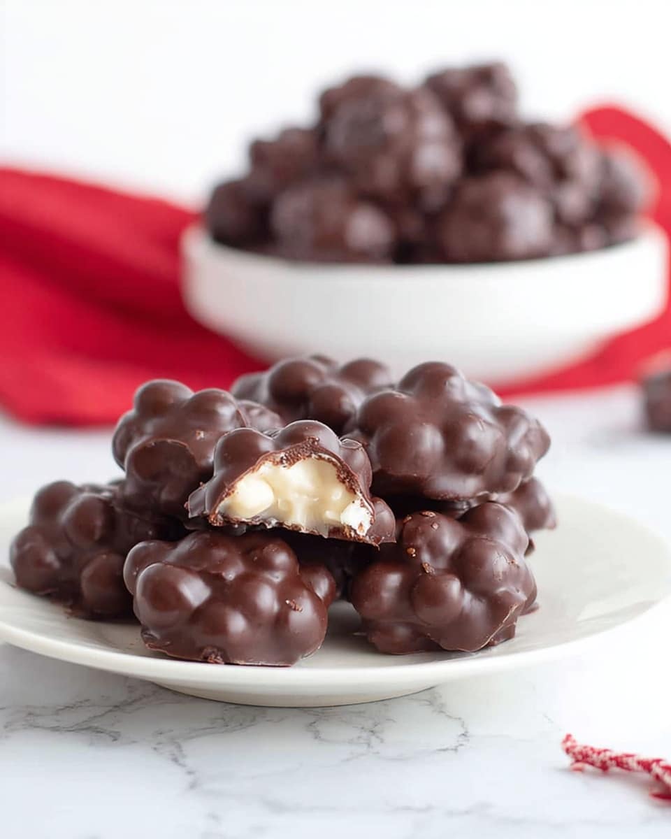 The image shows three clusters of dark chocolate-covered nuts stacked on a small white plate with a subtle black star pattern, placed on a sheet of light-colored parchment paper. Each cluster is made up of multiple round nut shapes coated in smooth, glossy dark chocolate, creating a bumpy texture. In the background, blurred chocolate clusters rest on the same white marbled surface, adding depth to the image. The overall tone is bright and clean with soft natural light highlighting the rich dark color of the chocolate. photo taken with an iphone --ar 4:5 --v 7