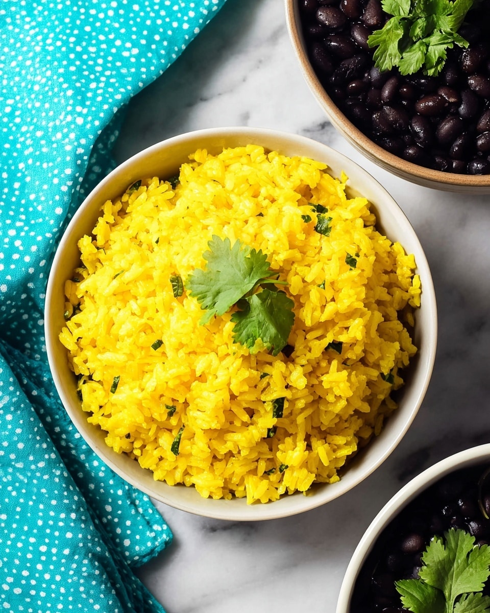A deep white bowl filled with a single layer of bright yellow rice mixed with small bits of green herbs scattered throughout, topped with a small sprig of fresh green cilantro in the center; in the background, slightly out of focus, there is another deep white bowl containing black beans with a few small green cilantro leaves on top; the setting is on a white marbled surface with a blurry patterned blue cloth and jars of spices in the background; the overall look is fresh and vibrant with contrasting colors. photo taken with an iphone --ar 4:5 --v 7