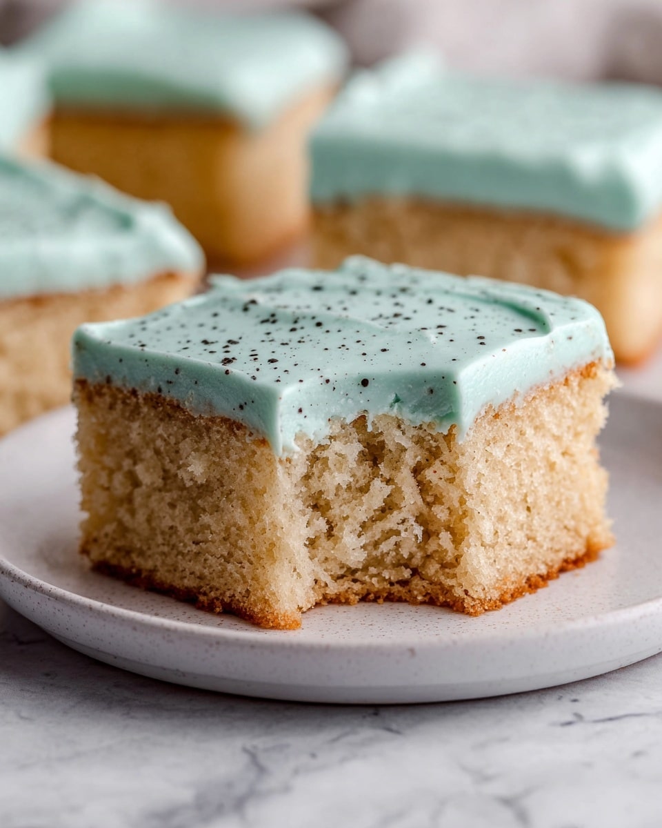 A square, golden-brown cake with a light blue creamy frosting being spread on top using a flat black spatula held by a woman's hand; the frosting is thick and smooth with soft swirls, covering the entire top of the cake and slightly spilling over the edges, all set on a piece of white parchment paper over a white marbled surface photo taken with an iphone --ar 4:5 --v 7