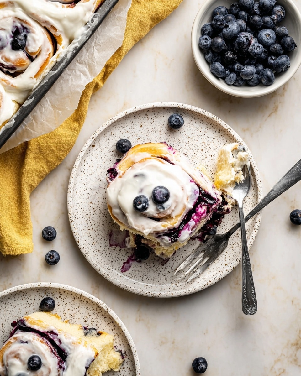 The image shows a close-up of a sweet roll cut open and placed on a white plate with speckled brown dots. The roll has two main layers: a soft, fluffy light beige bread layer on the outside and a dark purple-blueberry filling layer swirled inside, creating bright purple streaks. The top is covered with a thick layer of creamy white icing, slightly melting and dripping down the sides, mixed with bits of the blueberry filling. Some blueberries and a fork with pieces of roll are nearby on a white marbled texture surface, and a baking dish and bowl of blueberries are blurred in the background. Photo taken with an iphone --ar 4:5 --v 7