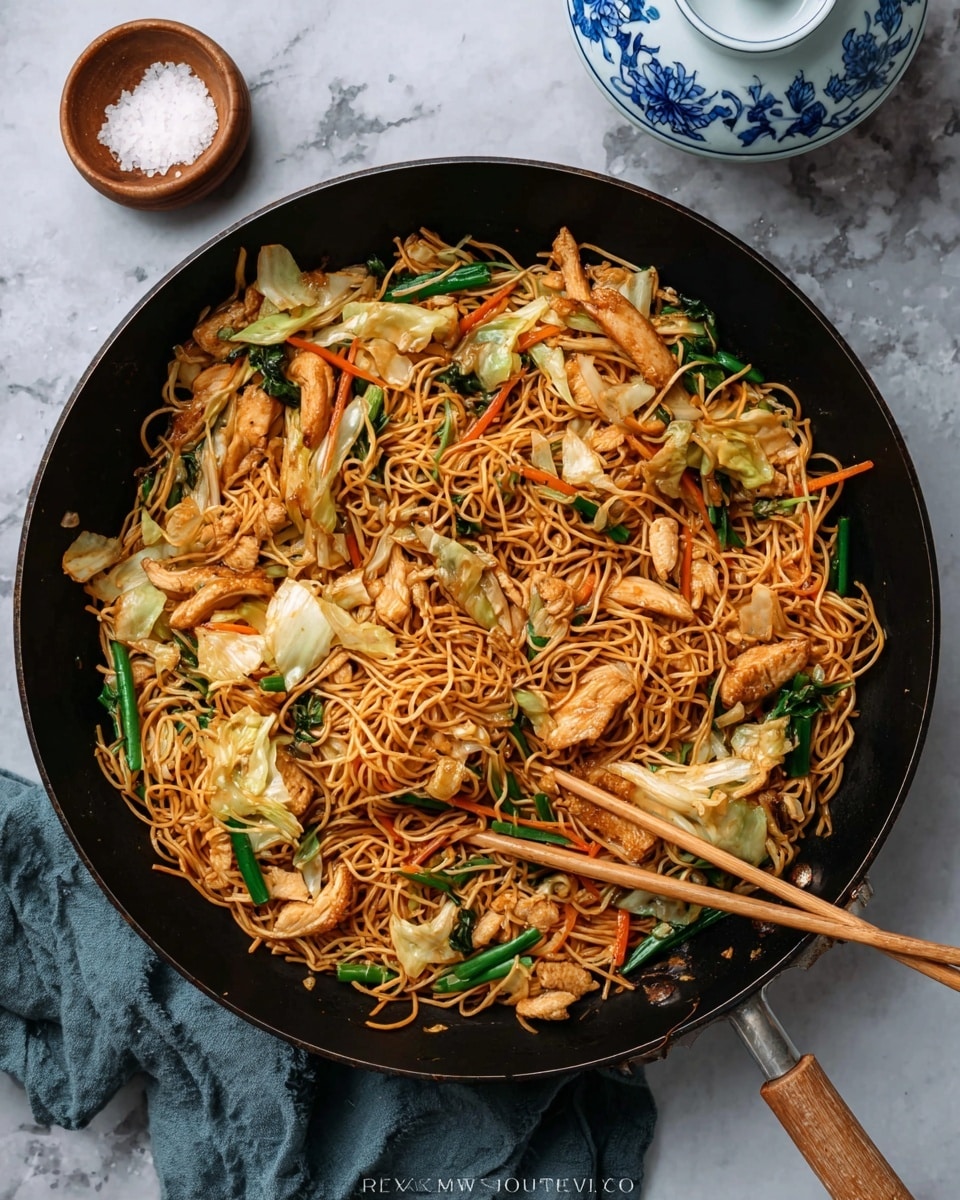 A black pan filled with cooked stir-fried noodles that are golden brown with a slightly oily texture, mixed with light brown pieces of cooked chicken scattered on top. There are thin strips of orange carrots, white and green pieces of cabbage, and green scallions mixed throughout the noodles. Two wooden chopsticks rest on the noodles near the bottom right part of the pan. The pan sits on a white marbled surface with a woman’s hand holding the pan handle on the lower left corner of the image. Photo taken with an iphone --ar 4:5 --v 7