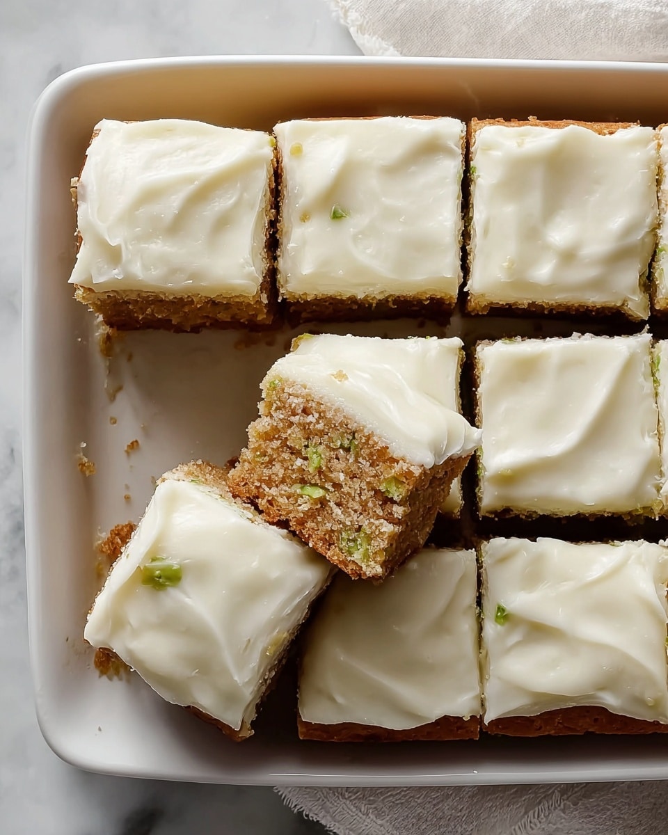 A close-up of a single cake piece on a white plate, showing two layers: the bottom layer is a moist, textured zucchini cake with visible green zucchini bits and a crumbly brown edge, and the top layer is a smooth, thick white frosting spread evenly over the cake. The background is a white marbled texture, softly blurred. photo taken with an iphone --ar 4:5 --v 7